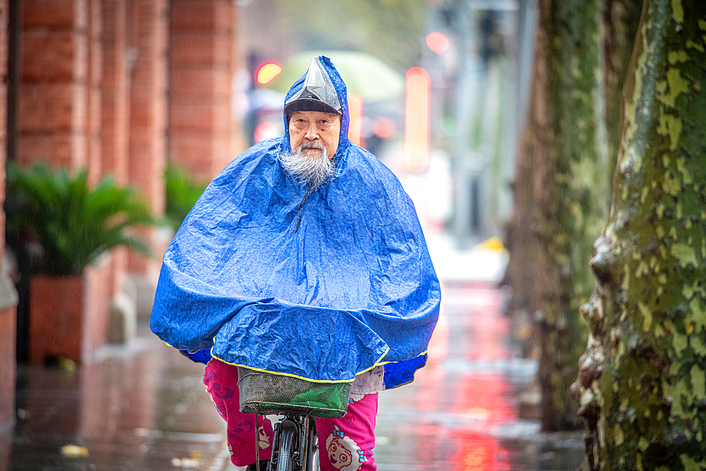 A determined older man rides his bike in the rain, Shanghai, China.