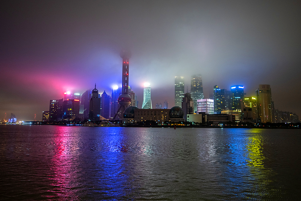 Mist lingers over the illuminated skyline of downtown Shanghai, China.