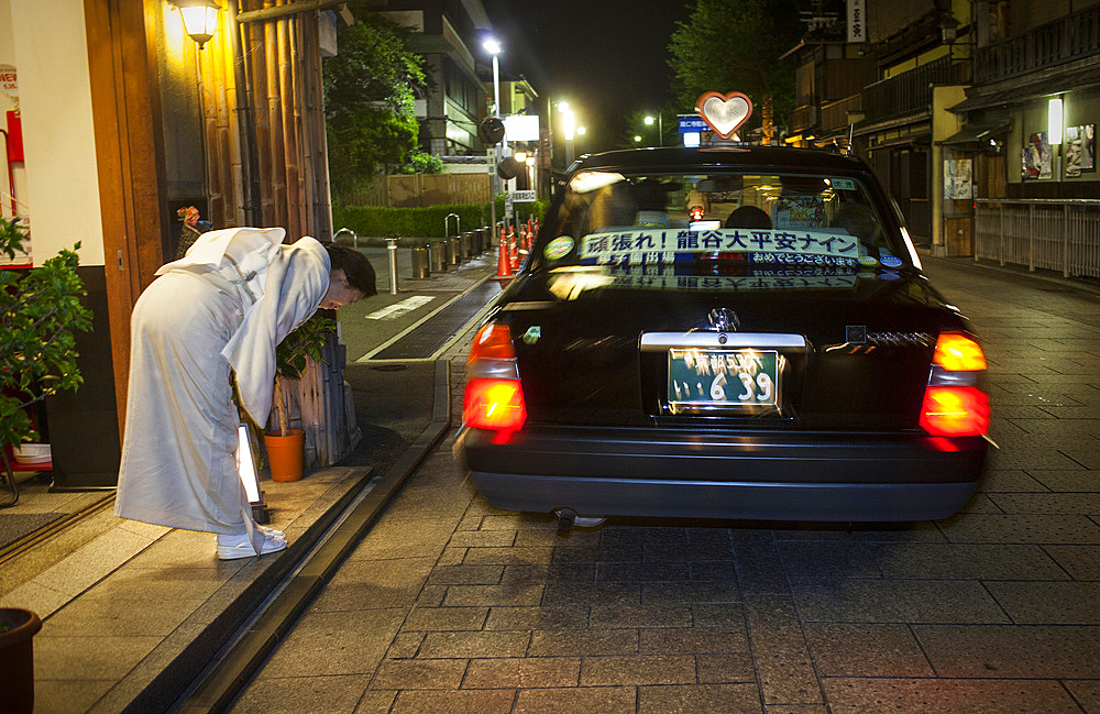 Oka san says goodbye to clients.Taxi in Hanamikoji dori street.Geisha's distric of Gion.Kyoto. Kansai, Japan.