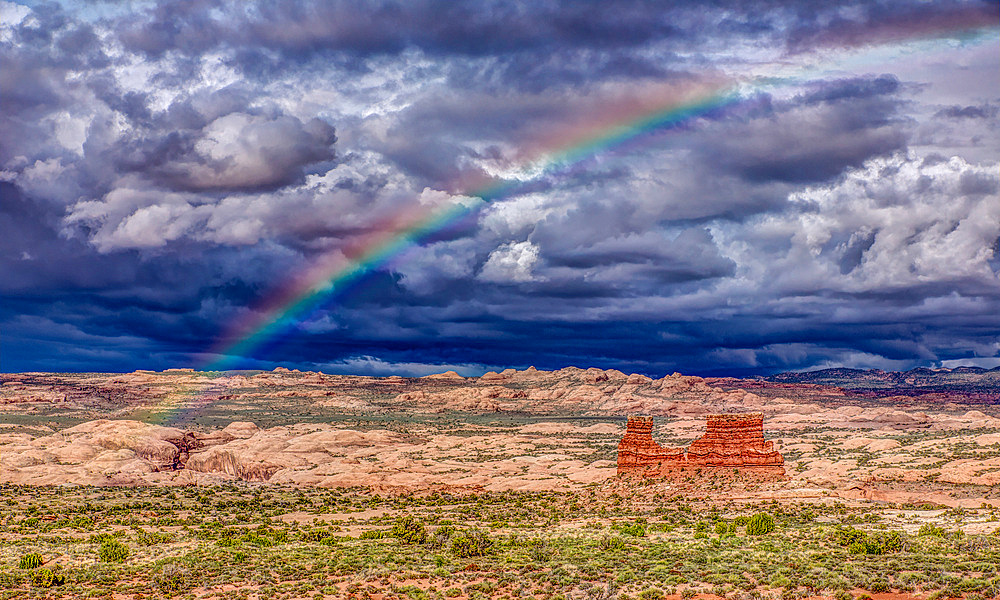 A rainbow over a sandstone monolith with stormy skies over Arches National Park, Moab, Utah.