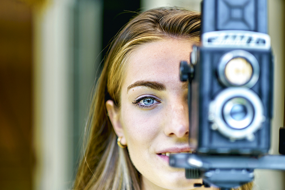 Portrait of a young beautiful caucasian woman in her 20´s with blue eyes photographing with an old vintage camera on a tripod outdoor. Lifestyle concept.