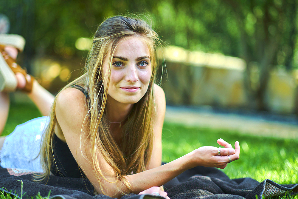 Portrait of a young beautiful caucasian woman in her 20s lying on the grass in a garden. Lifestyle concept.