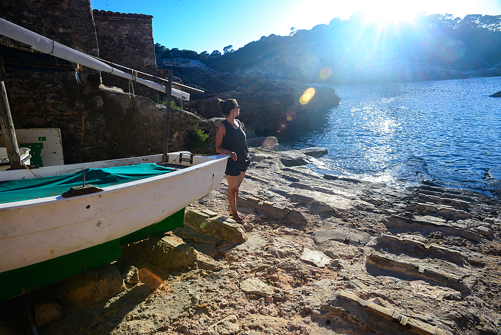 Young woman leaning on fishing boat on Cala SﾒAlmunia beach in Mallorca, Spain