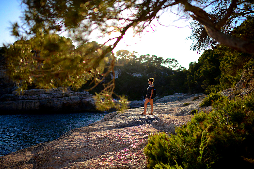 Young woman, surrounded by nature, looking at the horizon at sunset in the coast of Mallorca, Spain