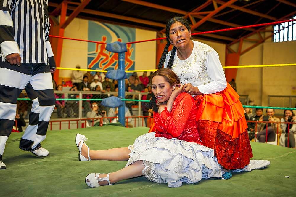 Lucha Libre. Combat between Dina with orange skirt and Benita la Intocable , cholitas females wrestlers ,with referee, Sports center La Ceja, El Alto, La Paz, Bolivia