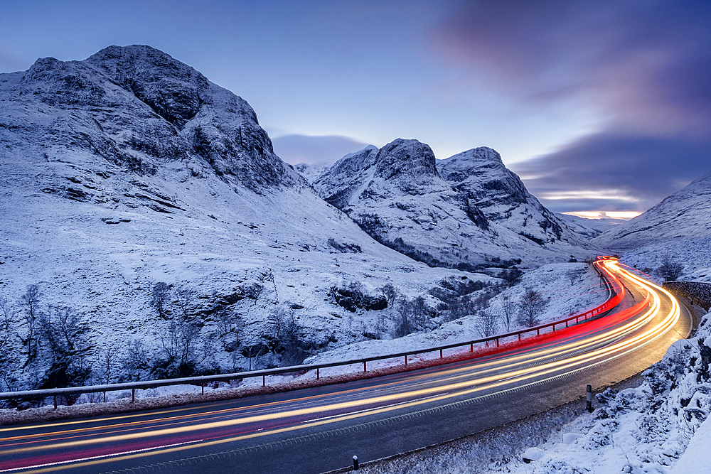 Traffic on the A82 road passing the snow covered Three Sisters of Glencoe, Aonach Dubh, Beinn Fhada and Gearr Aonach, at night in winter, Glencoe, Scottish Highlands, Scotland, United Kingdom, Europe