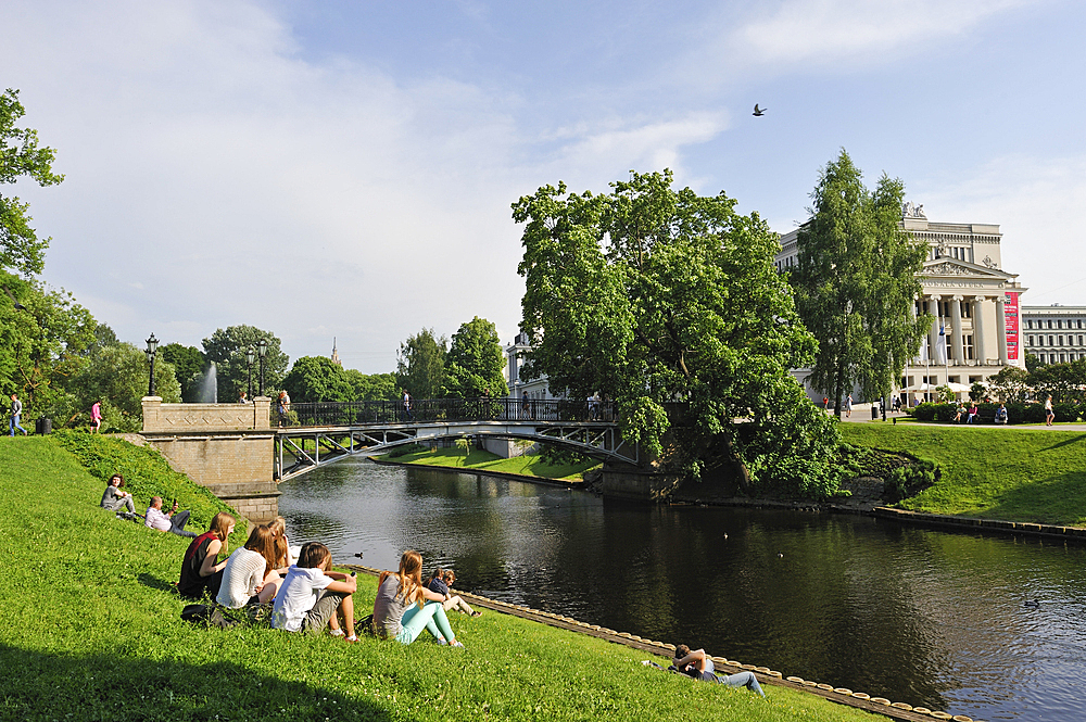 Young people on the bank of the Canal surrounding the Old Town of Riga, in front of the National Opera House, Riga, Latvia, Baltic region, Europe