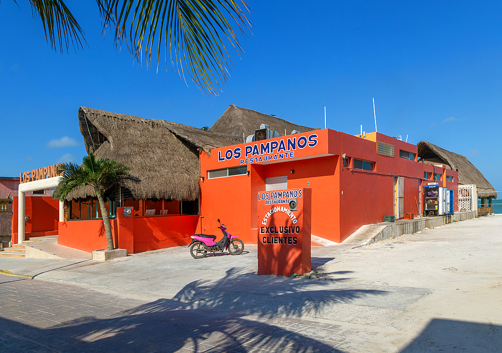 Thatched palapa roofed buildings and bright orange exterior of Los Pampanos seaside restaurant, Celestun, Yucatan, Mexico, North America