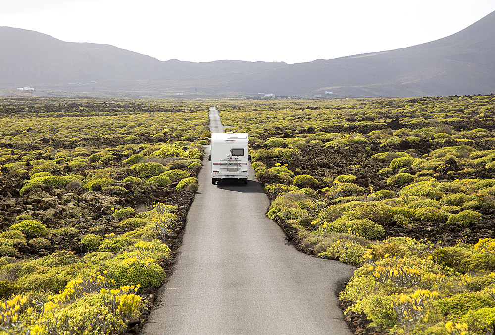 Motorhome on straight sealed tarmac road crossing lava flows, Malpais de Corona, Lanzarote, Canary Islands, Spain, Atlantic, Europe