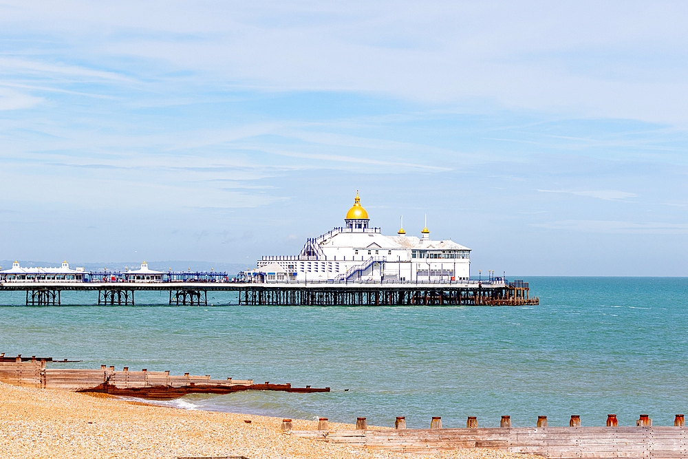 Serene beachscape with a classic pier extending into calm waters under a cloudy sky, with wooden groynes in the foreground, Eastbourne, Easts Sussex, England, United Kingdom, Europe