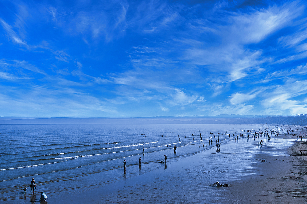 Scenic view of a tranquil beach with people strolling and the vast ocean meeting a blue sky with wispy clouds in Filey, England.