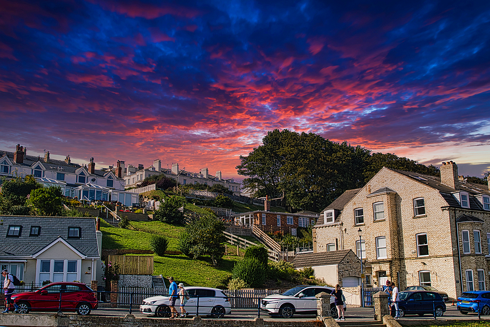 Quaint town at sunset with vibrant sky and traditional houses, parked cars in foreground in Filey, England.