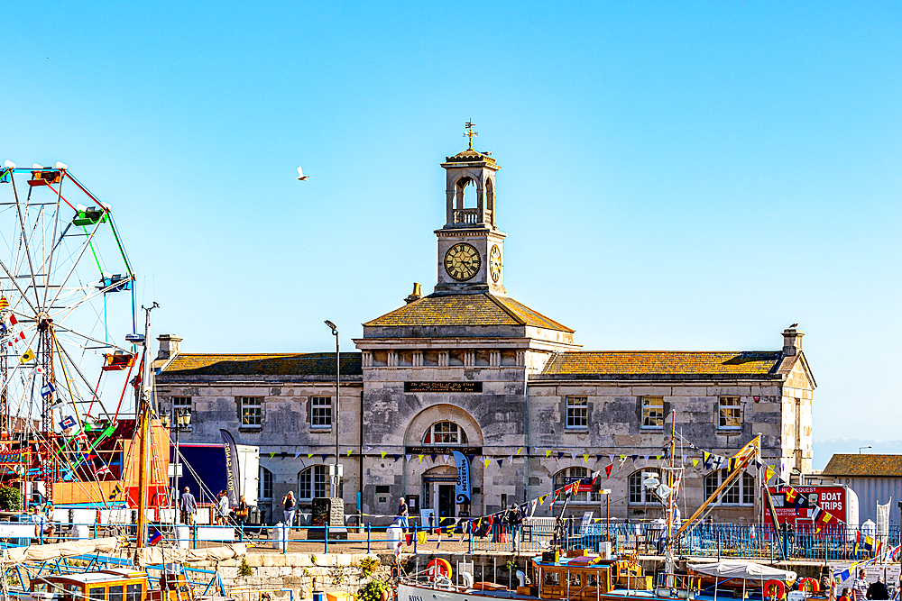 Historic building with clock tower near a ferris wheel under clear blue sky in Hastings, East Sussex, England, United Kingdom, Europe