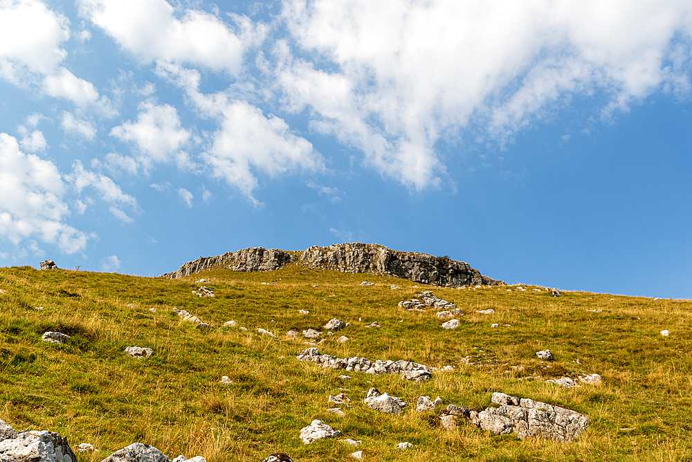 Sunny landscape of a grassy hill with rocky outcrop under a blue sky with clouds, North Yorkshire, England, United Kingdom, Europe