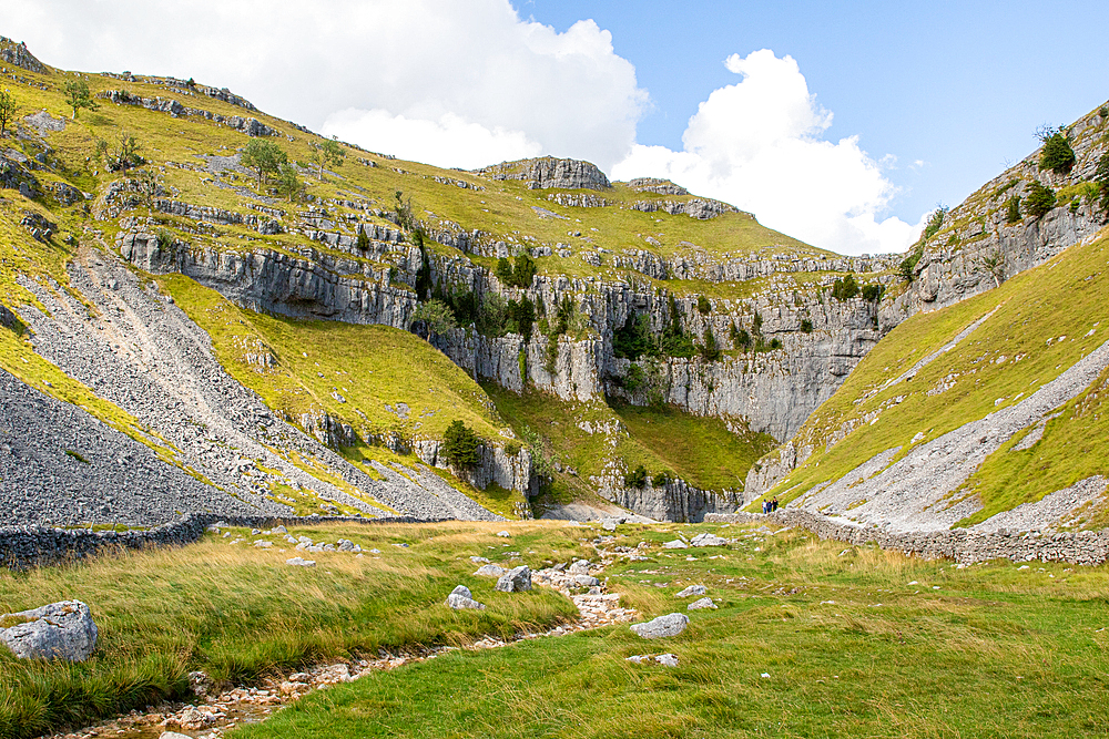 Scenic limestone cliffs with grassy slopes and rocky terrain under a cloudy sky in a mountainous region, North Yorkshire, England, United Kingdom, Europe