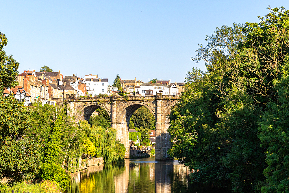 Scenic view of a historic stone bridge over a calm River Nidd, surrounded by lush greenery and a clear blue sky, Knaresborough, North Yorkshire, England, United Kingdom, Europe