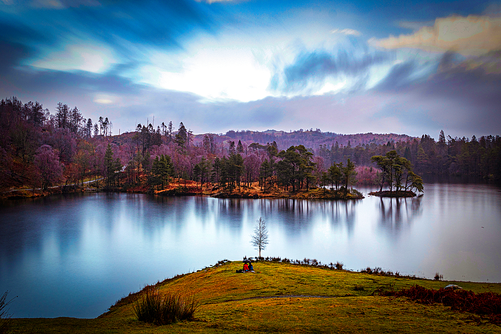 Serene lake with reflection of autumn trees under a dynamic blue sky with clouds at dusk in the Lake District, Cumbria, England, United Kingdom, Europe