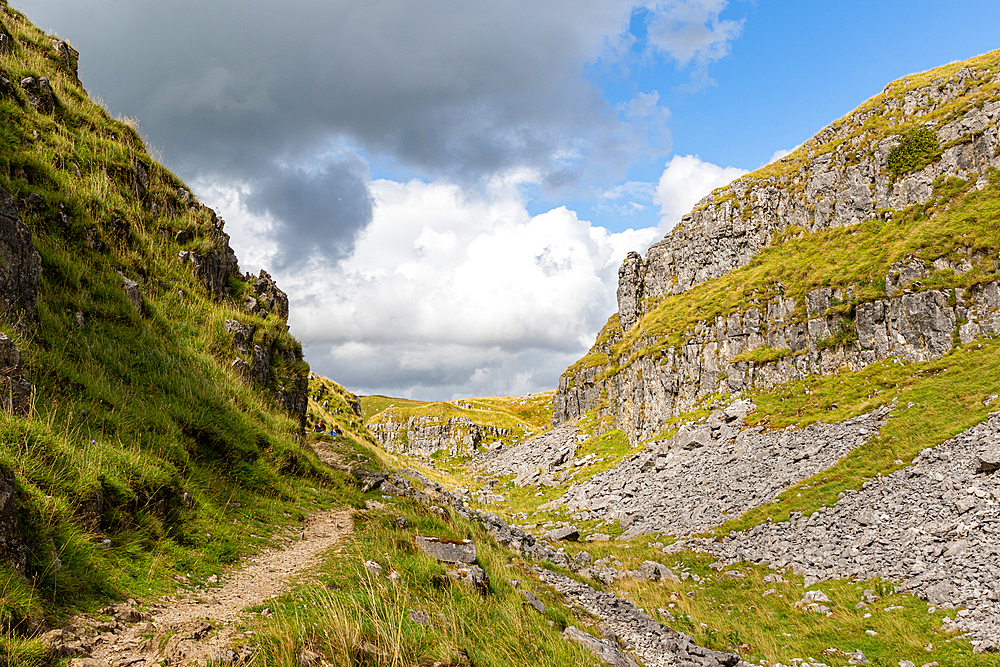 Scenic view of a mountain path with lush greenery under a cloudy sky at Malham Cove, Yorkshire, England, United Kingdom, Europe