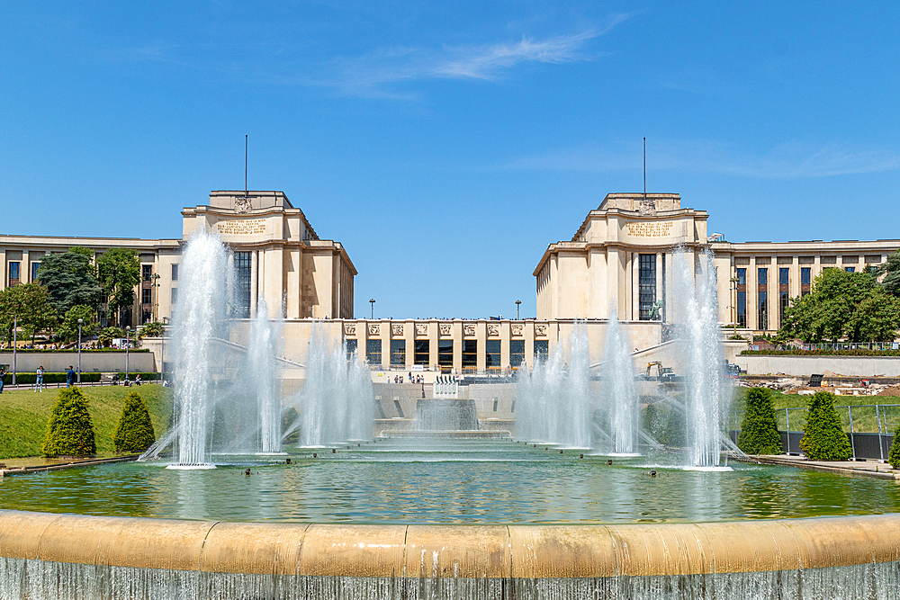 Symmetrical view of a grand fountain with water jets in front of a classical building under a clear blue sky, Paris, France, Europe