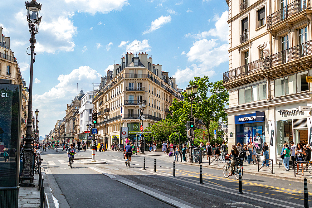 Sunny day on a bustling city street with pedestrians and cyclists, classic architecture, and clear blue sky, Paris, France, Europe