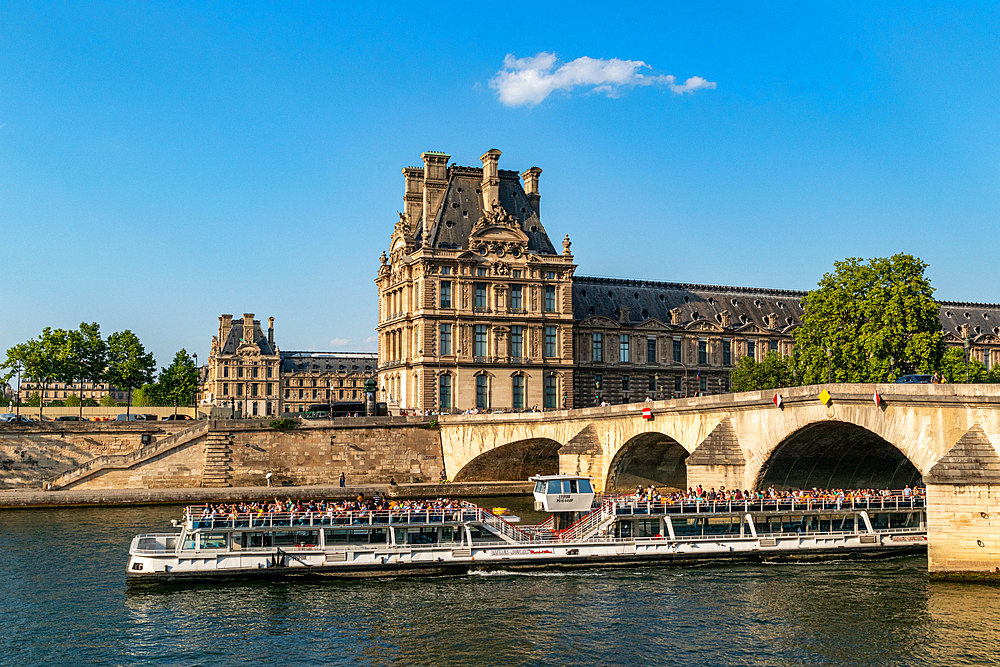 Scenic view of a river cruise boat passing under a bridge o the River Seine, near a historic building on a sunny day, Paris, France, Europe