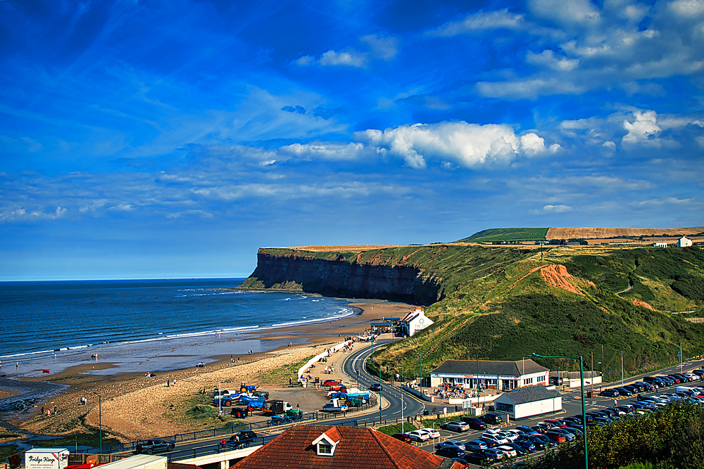 Sunny coastal landscape with cliff, beach, and winding road leading to a small seaside village in Saltburn-by-the-Sea, England.