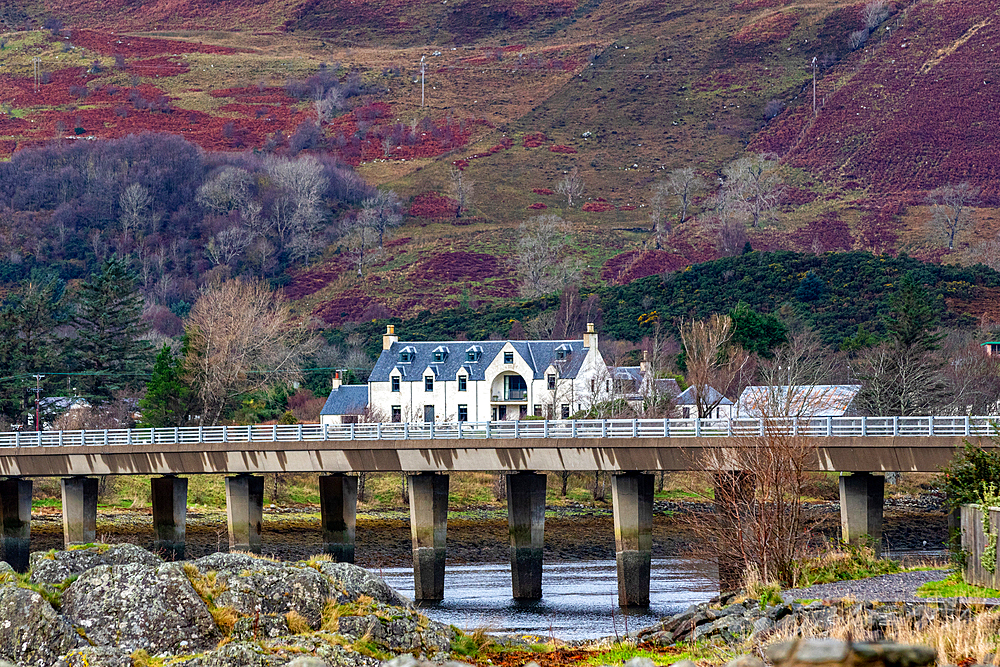 Quaint white house with a slate roof behind a stone bridge over a tranquil river, set against a backdrop of rolling hills and sparse woodland in Scotland, United Kingdom, Europe