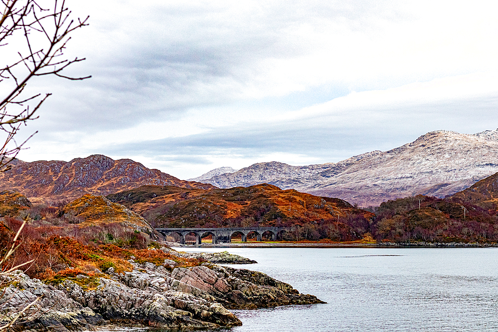 Serene landscape with a tranquil lake, autumnal trees, and distant snow-capped mountains under a cloudy sky in Scotland, United Kingdom, Europe