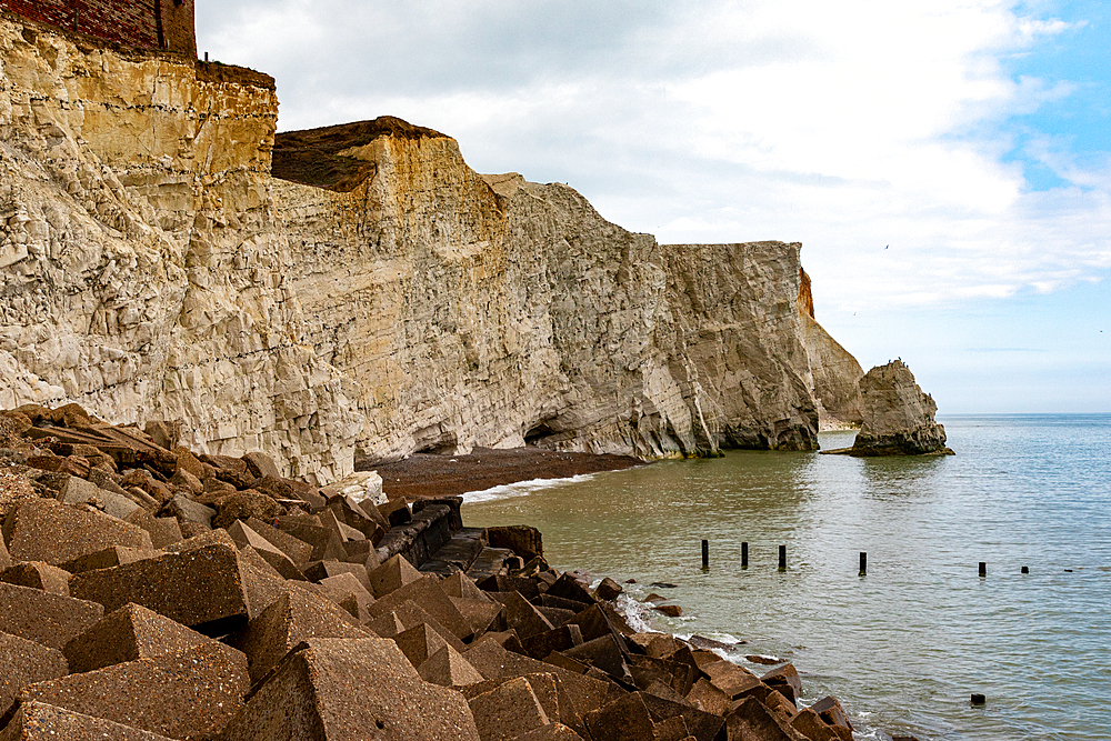 Dramatic chalk cliffs with boulder-strewn beach and calm sea under a cloudy sky, Staithes, Yorkshire, England, United Kingdom, Europe
