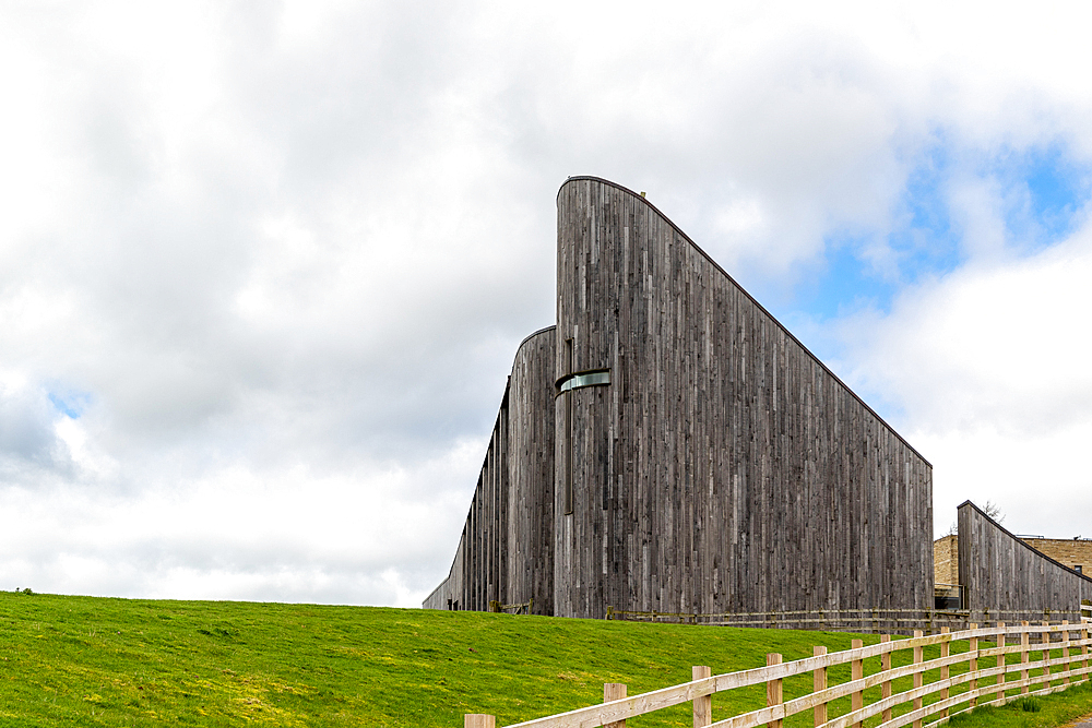 Modern wooden architecture with curved design against a cloudy sky, surrounded by green grass and a fence, North York Moors, Yorkshire, England, United Kingdom, Europe United Kingdom, Europe