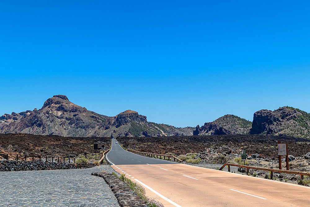 Desert road stretching into the distance with rocky mountains under a clear blue sky in Tenerife, Canary Islands, Spain, Atlantic, Europe