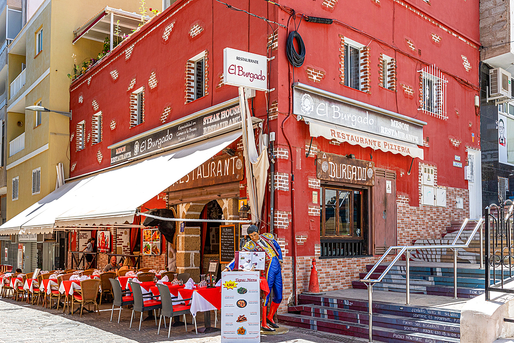 Cosy street cafe with red chairs and umbrellas in front of a traditional red building on a sunny day in Los Cristianos, Tenerife, Canary Islands, Spain, Atlantic, Europe