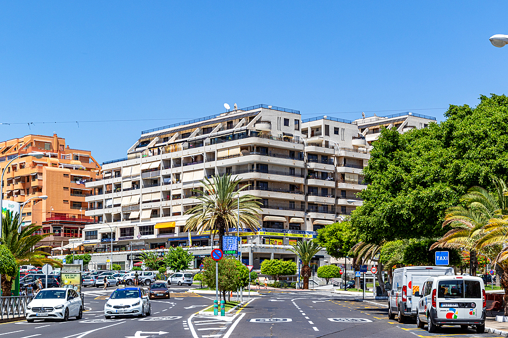 Urban street scene with modern apartment buildings, lush green trees, and cars on a sunny day in Los Cristianos, Tenerife, Canary Islands, Spain, Atlantic, Europe