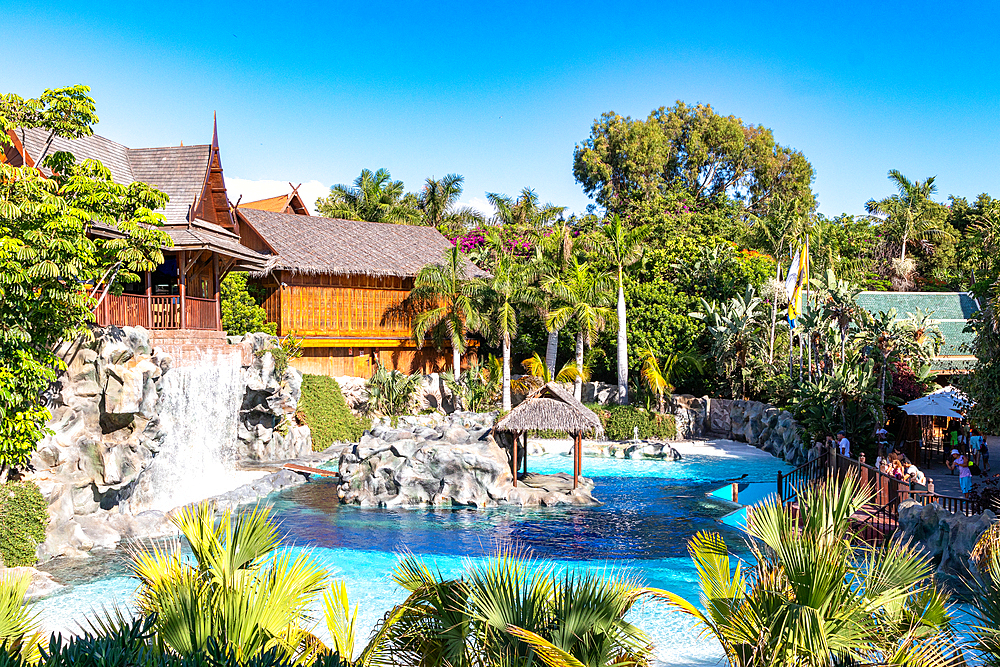 Tropical resort with swimming pool, waterfall, and traditional huts surrounded by lush greenery at Siam Park in Tenerife, Canary Islands, Spain, Atlantic, Europe