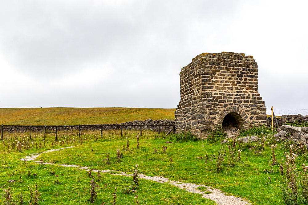 Old stone lime kiln on a grassy field with a cloudy sky, path leading to the historical structure, North Yorkshire, England, United Kingdom, Europe