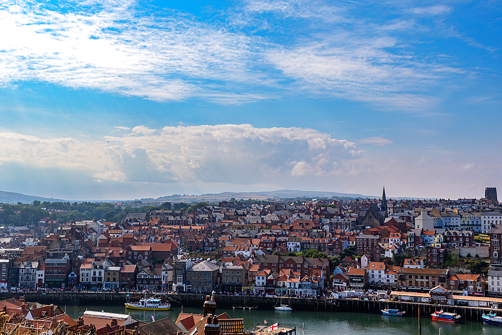 Aerial view of a coastal town with historic buildings, a riverfront, and boats under a blue sky with clouds in Whitby, Yorkshire, England, United Kingdom, Europe