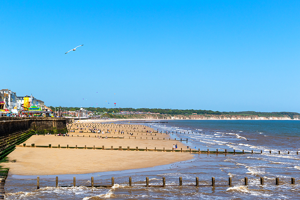 Sunny beach scape with wooden pier, colorful buildings, and people enjoying the shore, clear blue sky above in Bridlington, Yorkshire, England, United Kingdom, Europe