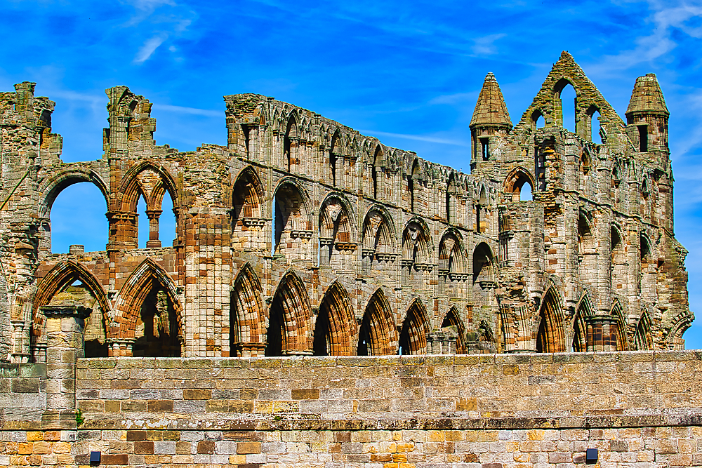 A historic stone abbey ruin with arched windows and intricate architectural details against a blue sky.