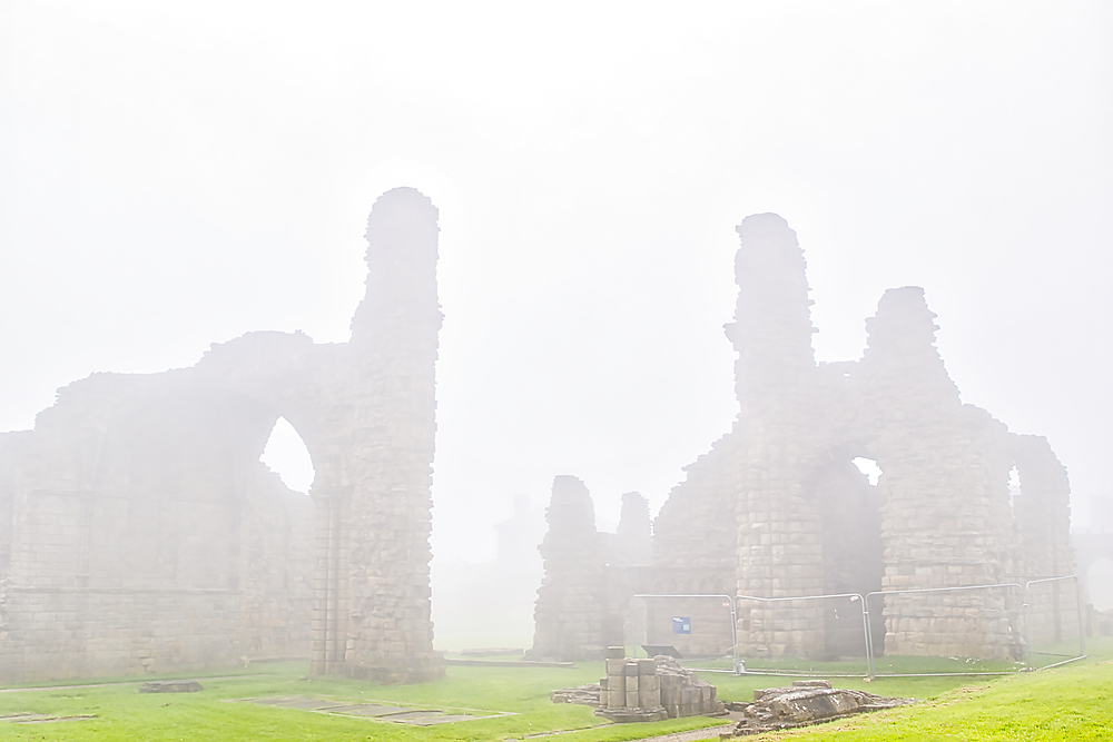 Ruins of an ancient stone structure shrouded in dense fog, with green grass in the foreground.