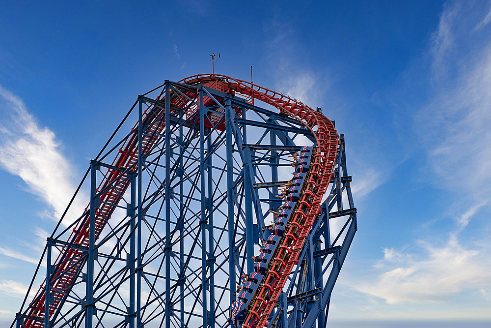 A towering roller coaster track ascending into a clear blue sky with wispy clouds, showcasing the intricate steel structure and vibrant red track.