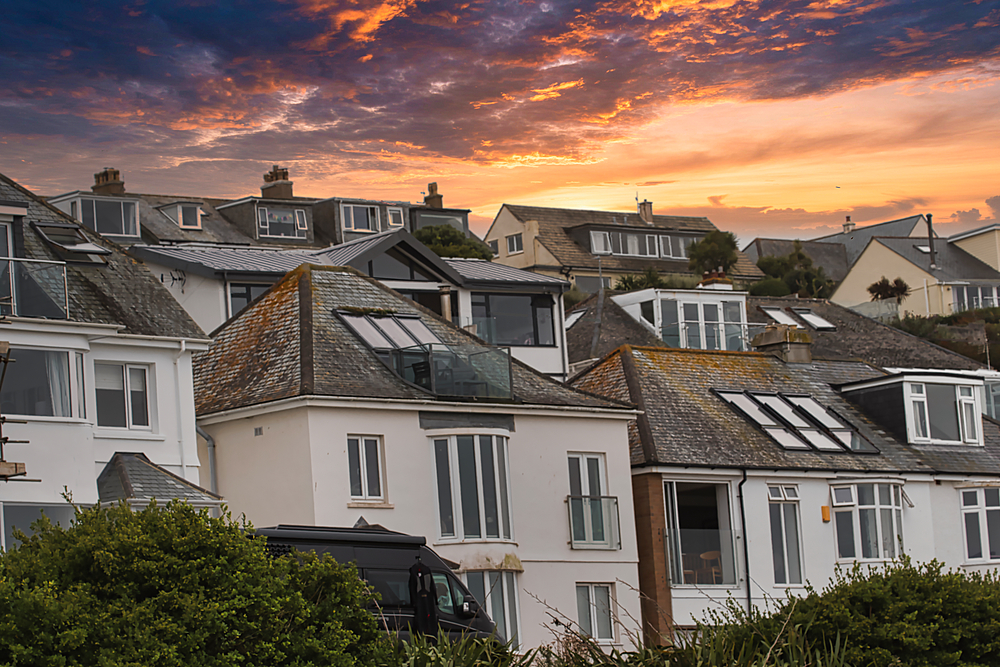 A picturesque view of coastal houses at sunset, showcasing a mix of modern and traditional architecture. The sky is filled with vibrant colors, creating a serene atmosphere.