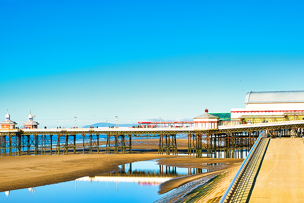 Serene seaside pier with clear blue sky reflected in calm water, showcasing tranquil coastal scenery in Blackpool, England