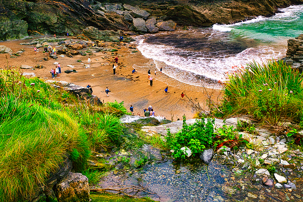 A scenic beach view with people enjoying the sandy shore, surrounded by rocky cliffs and lush greenery. The turquoise waves gently lap at the beach, creating a tranquil atmosphere.