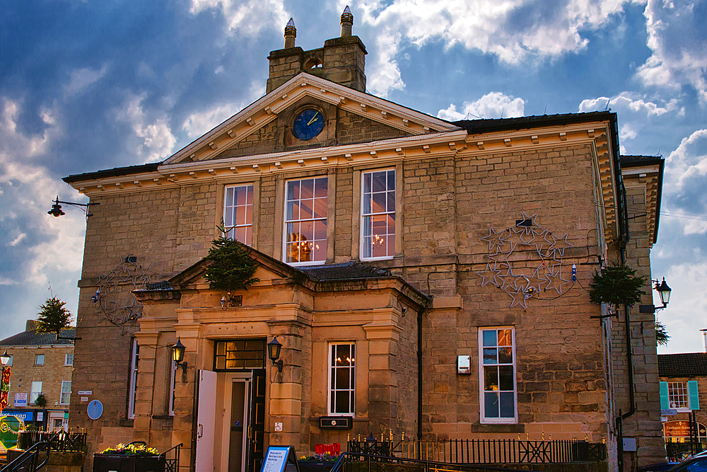 A tan stone building with a clock in the pediment, multiple windows, and decorative metalwork. A black wrought iron fence is visible in the foreground. The building has a classical architectural style in Wetherby, UK.