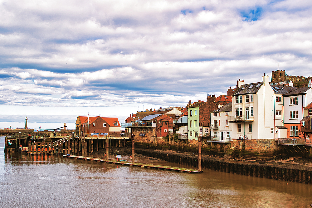 Whitby cityscape view with buildings, pier, and water under a cloudy sky.