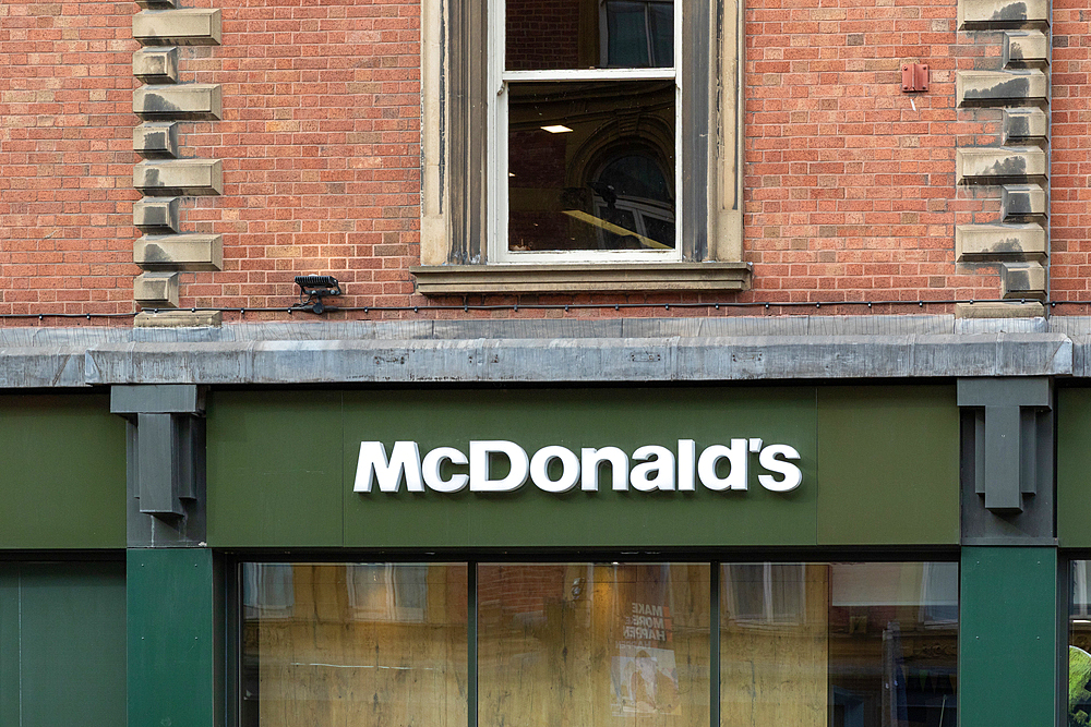 Close-up of a McDonald's restaurant sign on a brick building. The sign is green with white lettering. The image is shot during the day in Leeds, UK.