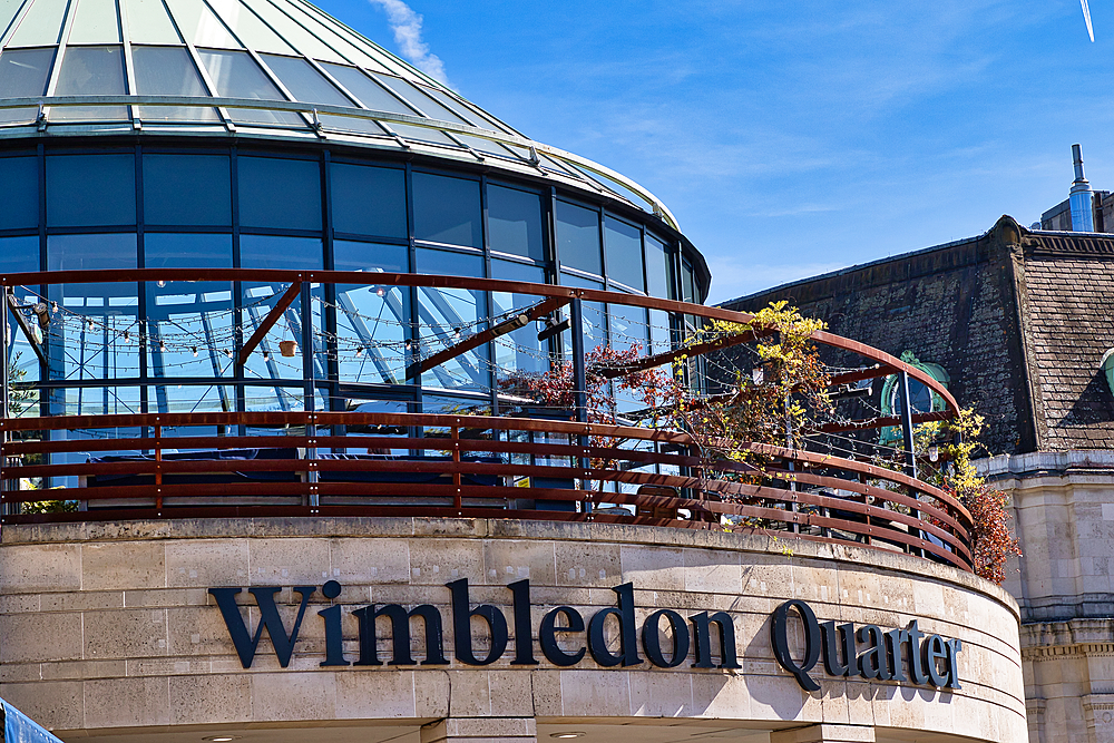 Exterior shot of the Wimbledon Quarter building, featuring a glass dome, balcony with string lights, and stone facade with signage.
