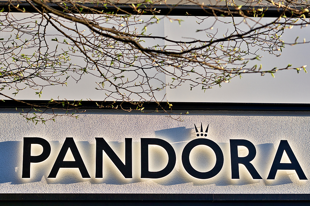 Pandora sign on a white textured wall with branches and budding leaves in the foreground in Harrogate, Yorkshire, UK.