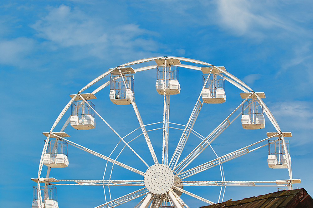 Partial view of a white Ferris wheel against a bright blue sky with some wispy clouds. The bottom of the wheel is partially obscured at Sandhaven Beach, UK