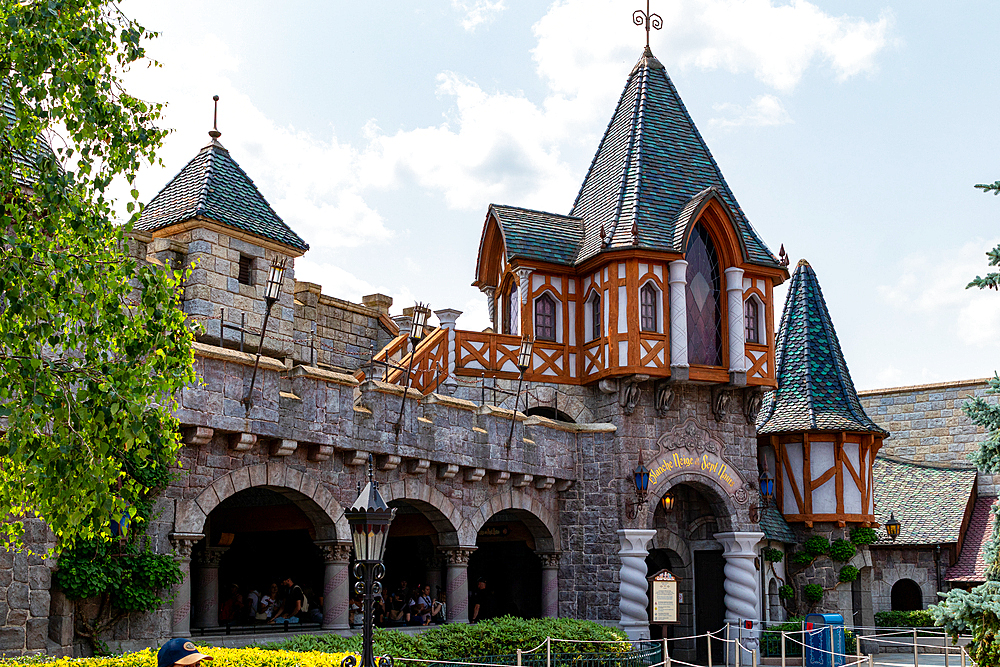 Exterior view of a building with stone facade, towers, arches, and a sign reading 'Blanche Neige et Sept Nains. at Disneyland Paris.